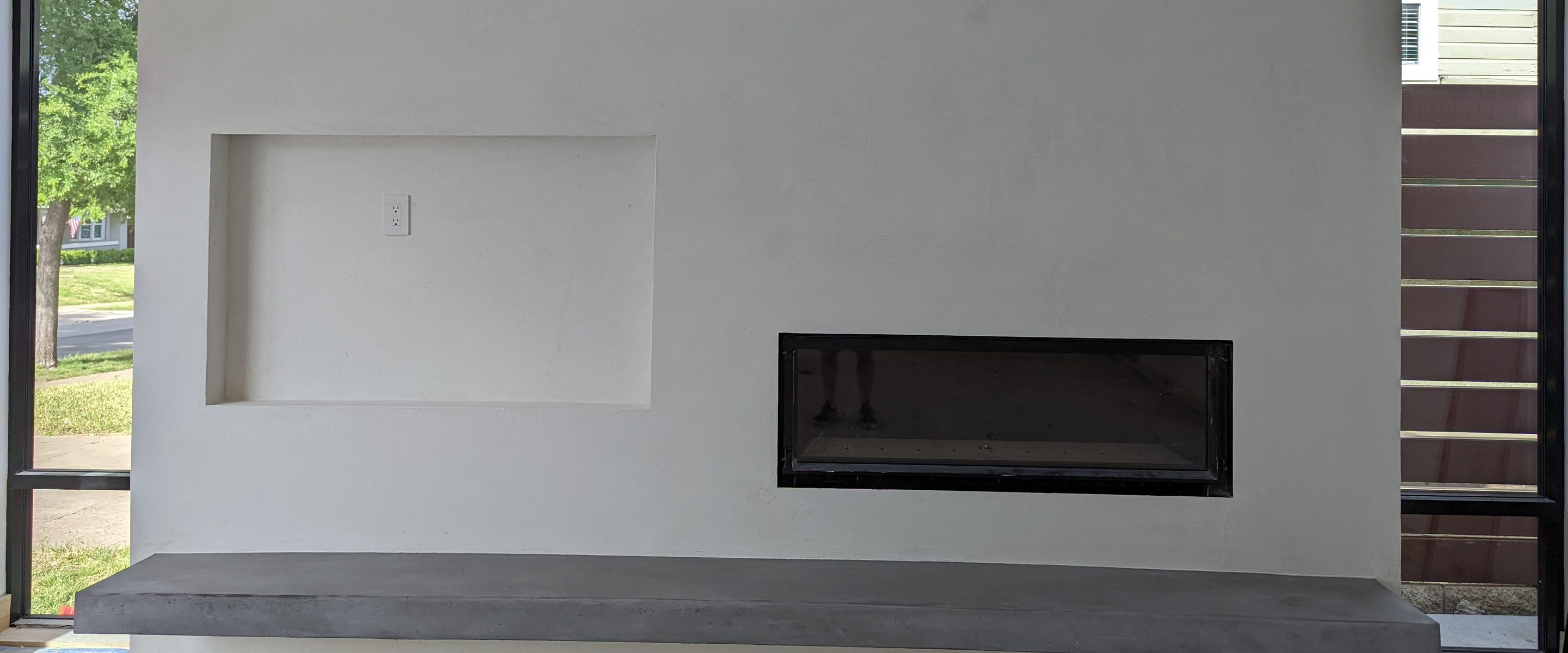 A modern white fireplace wall between tall black-framed windows.