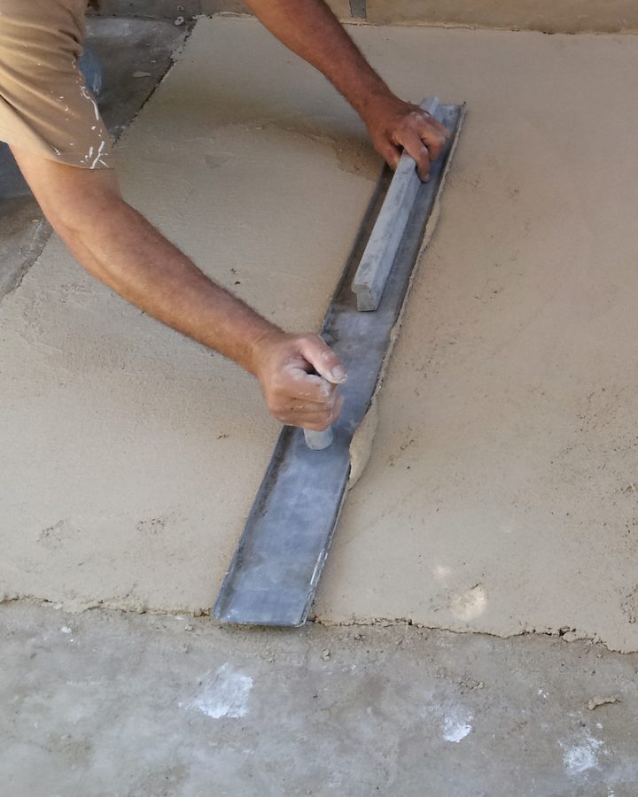 An applicator's arms drawing a straightedge across fresh plaster.