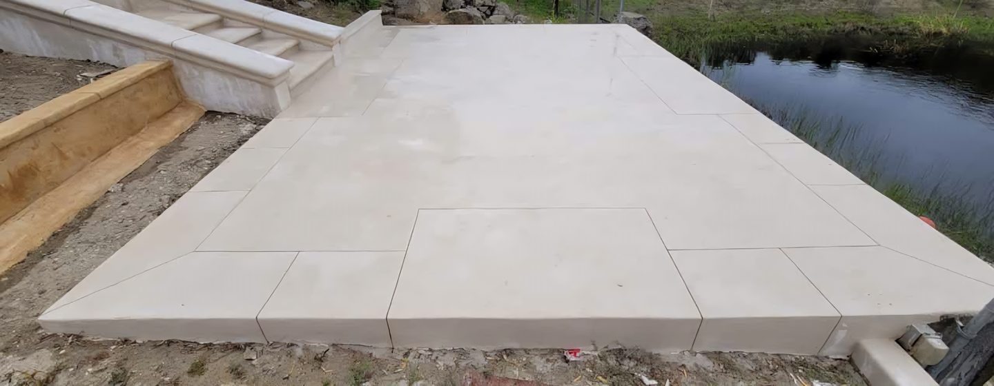 A terrace of pale coated slabs beside a pond.
