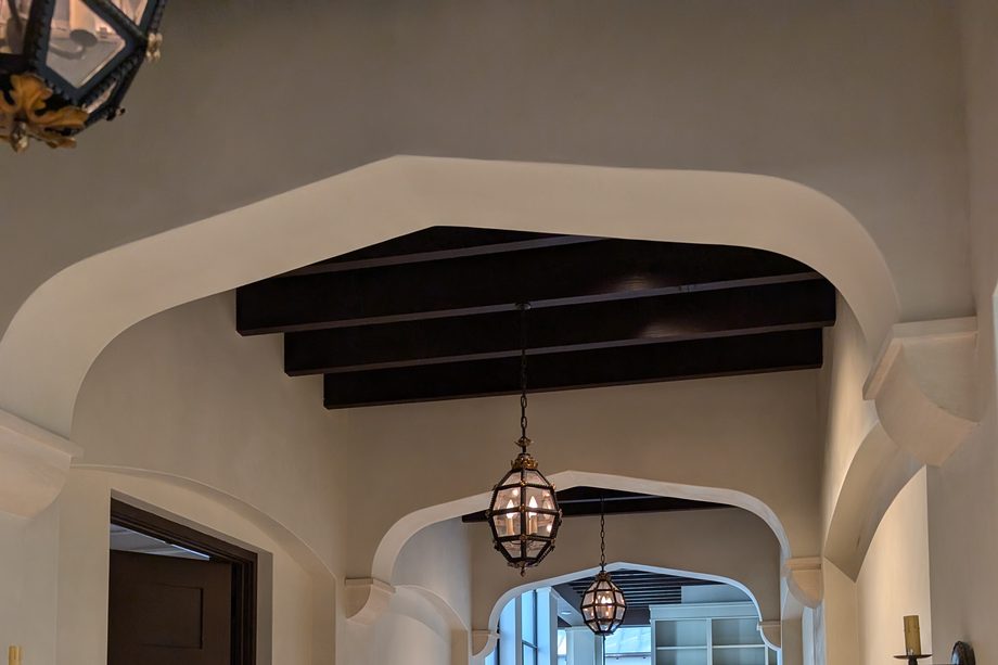 A hallway of shaped cream arches under dark ceiling beams.