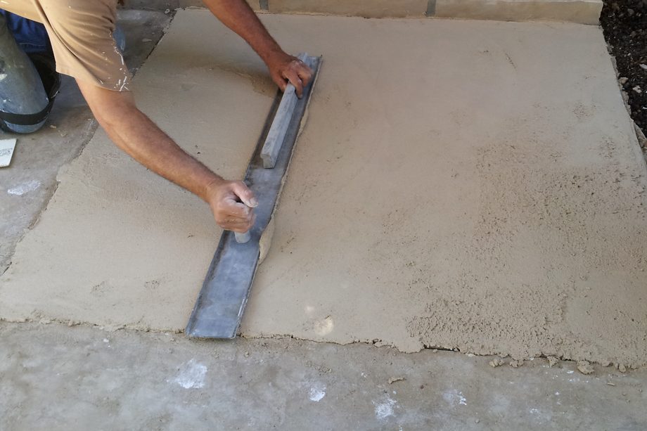 An applicator's arms drawing a straightedge across fresh plaster.