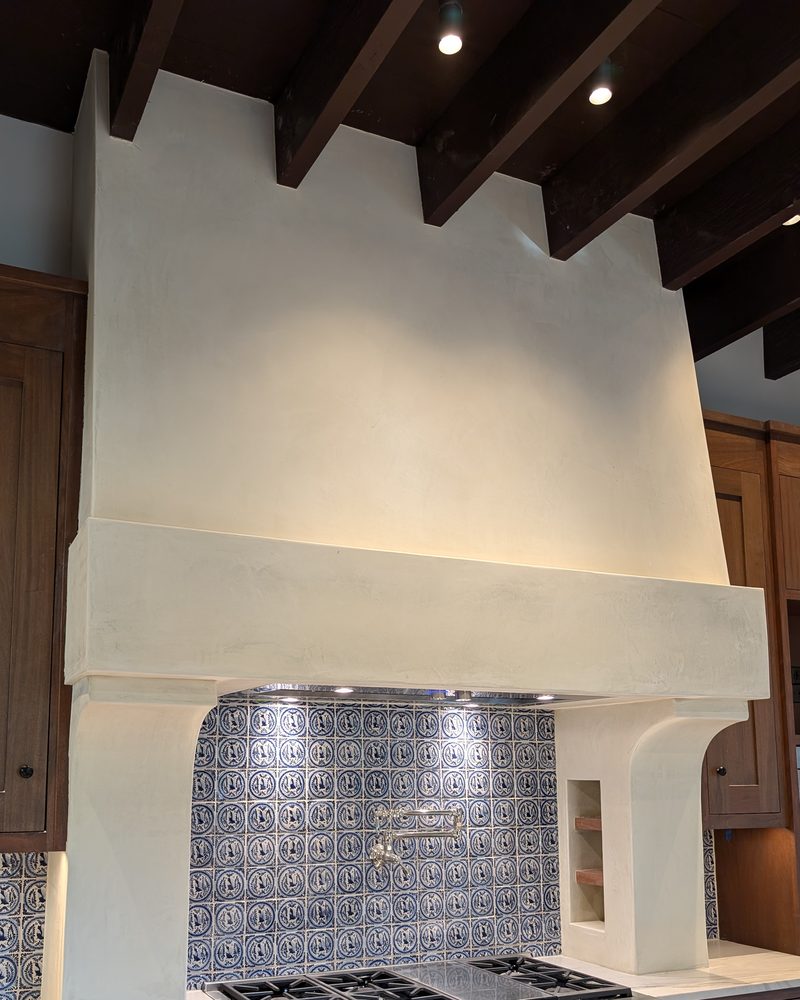 A large cream range hood under dark ceiling beams.