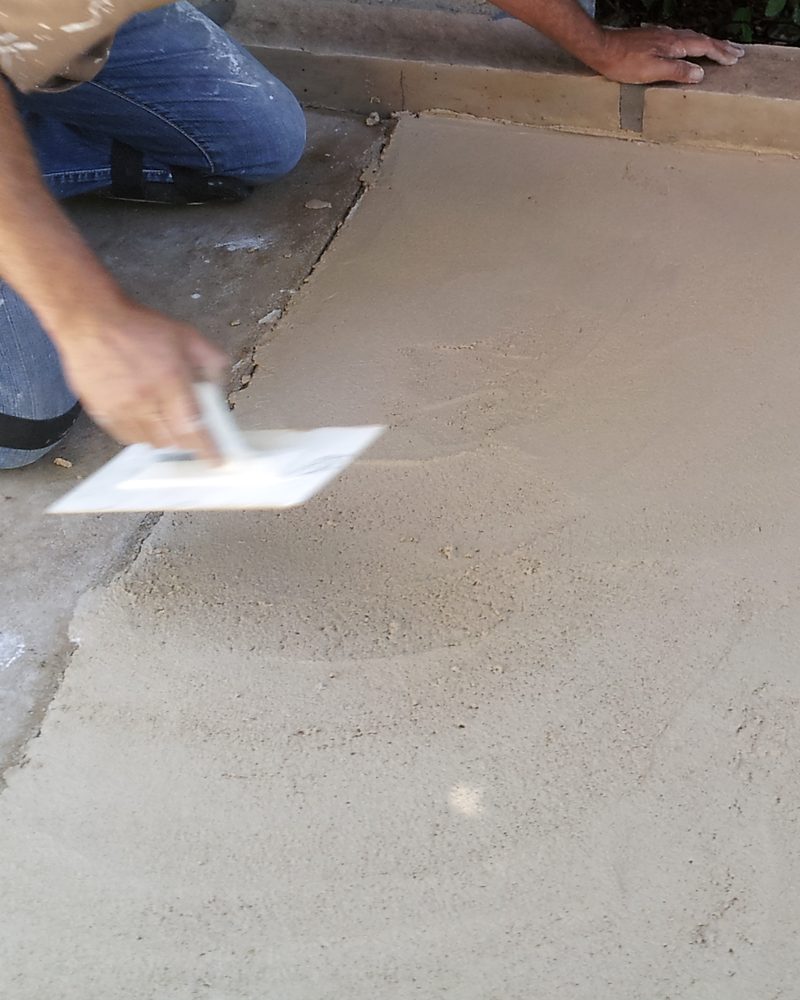 An applicator's hands floating a fresh coating on a slab.