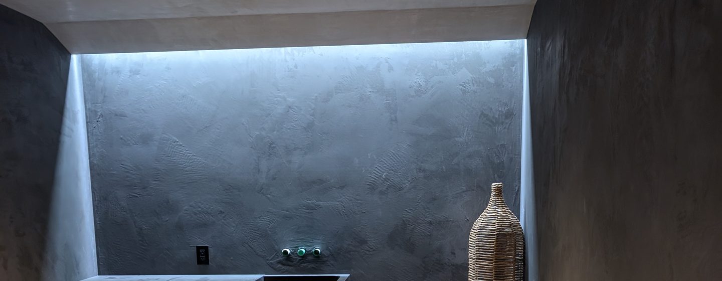 A dark coated room with a lit niche above a low cabinet.