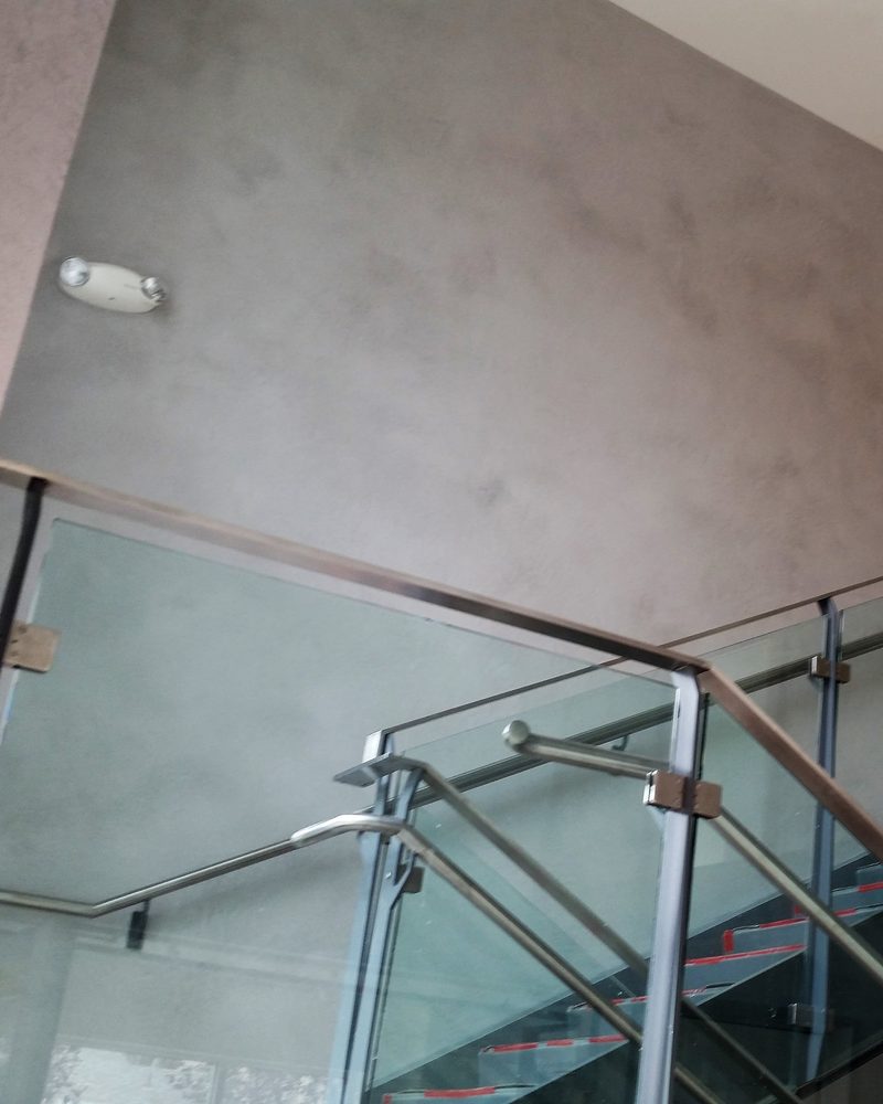 A grey coated stair-hall wall above a glass railing.
