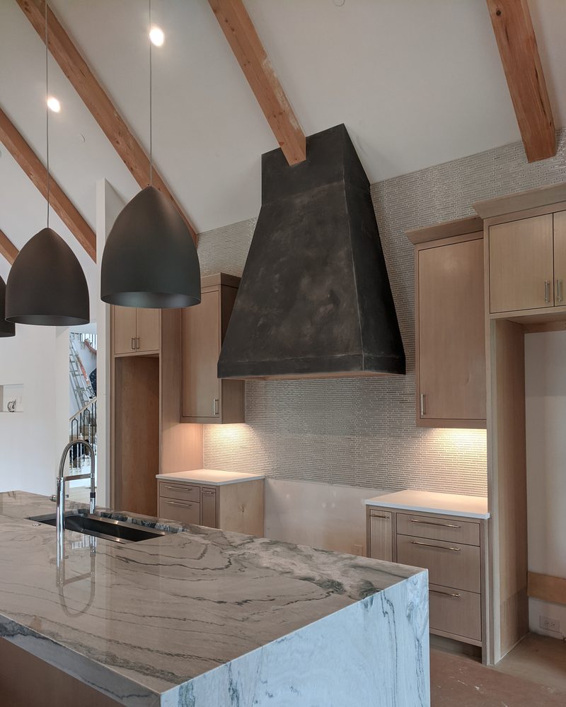 A dark coated range hood in a modern kitchen with a marble island.