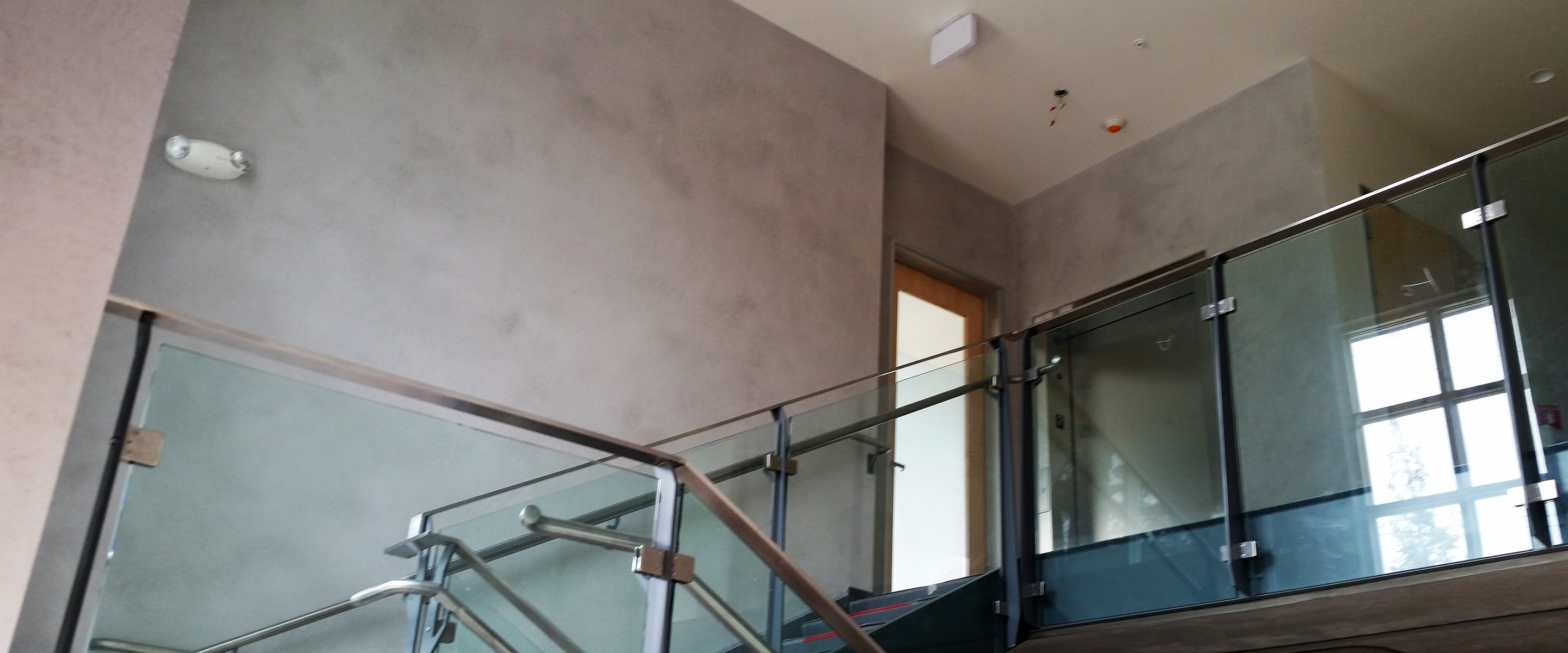 A grey coated stair-hall wall above a glass railing.