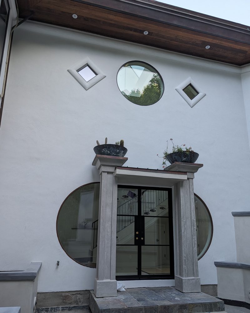 A white entry court with round windows and a coated-stone door surround.