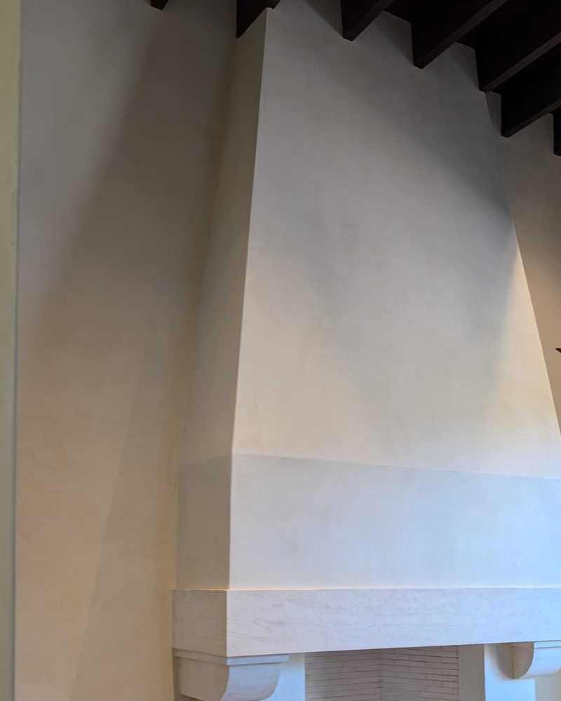 A tall smooth cream fireplace hood in a room with dark beams.