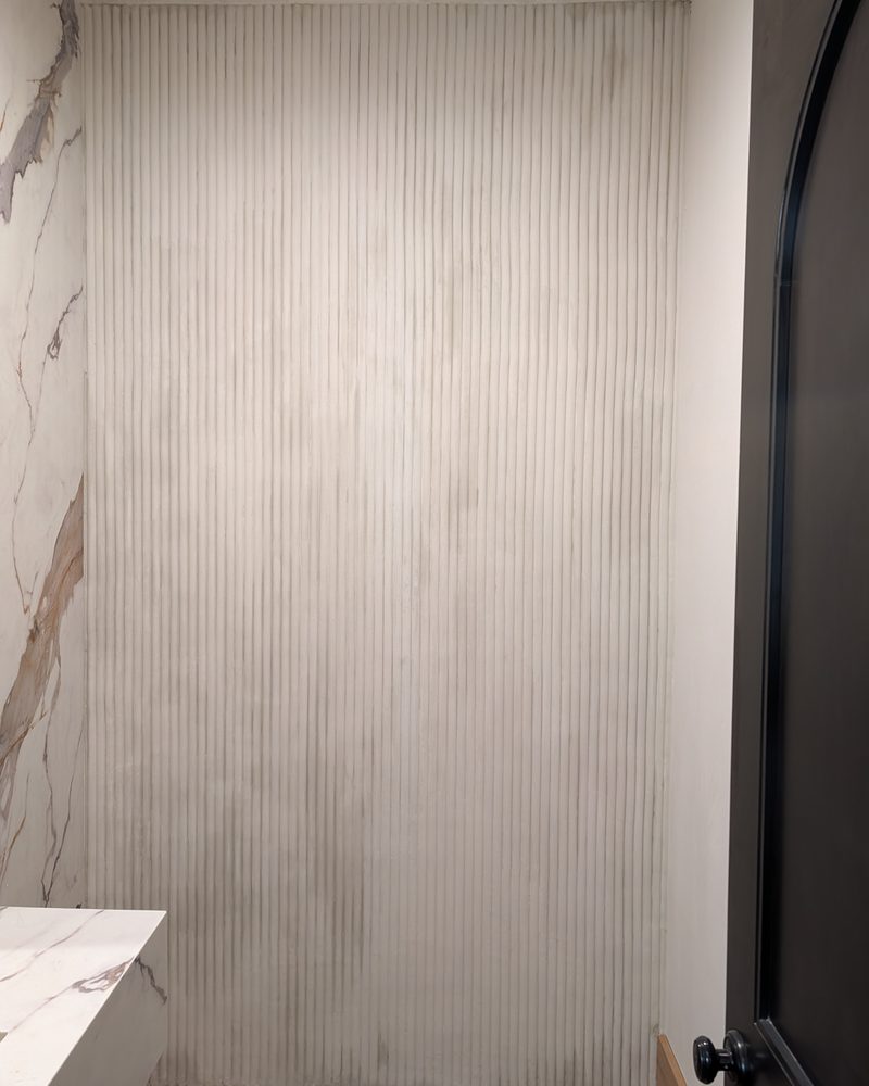 A floor-to-ceiling fluted wall in pale coated stone.