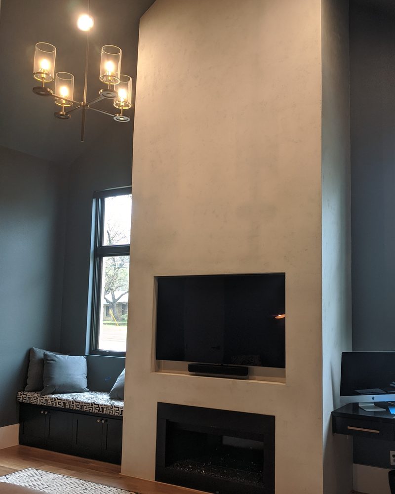 A tall fireplace wall in smooth pale Marblecoat, in a room with dark walls.