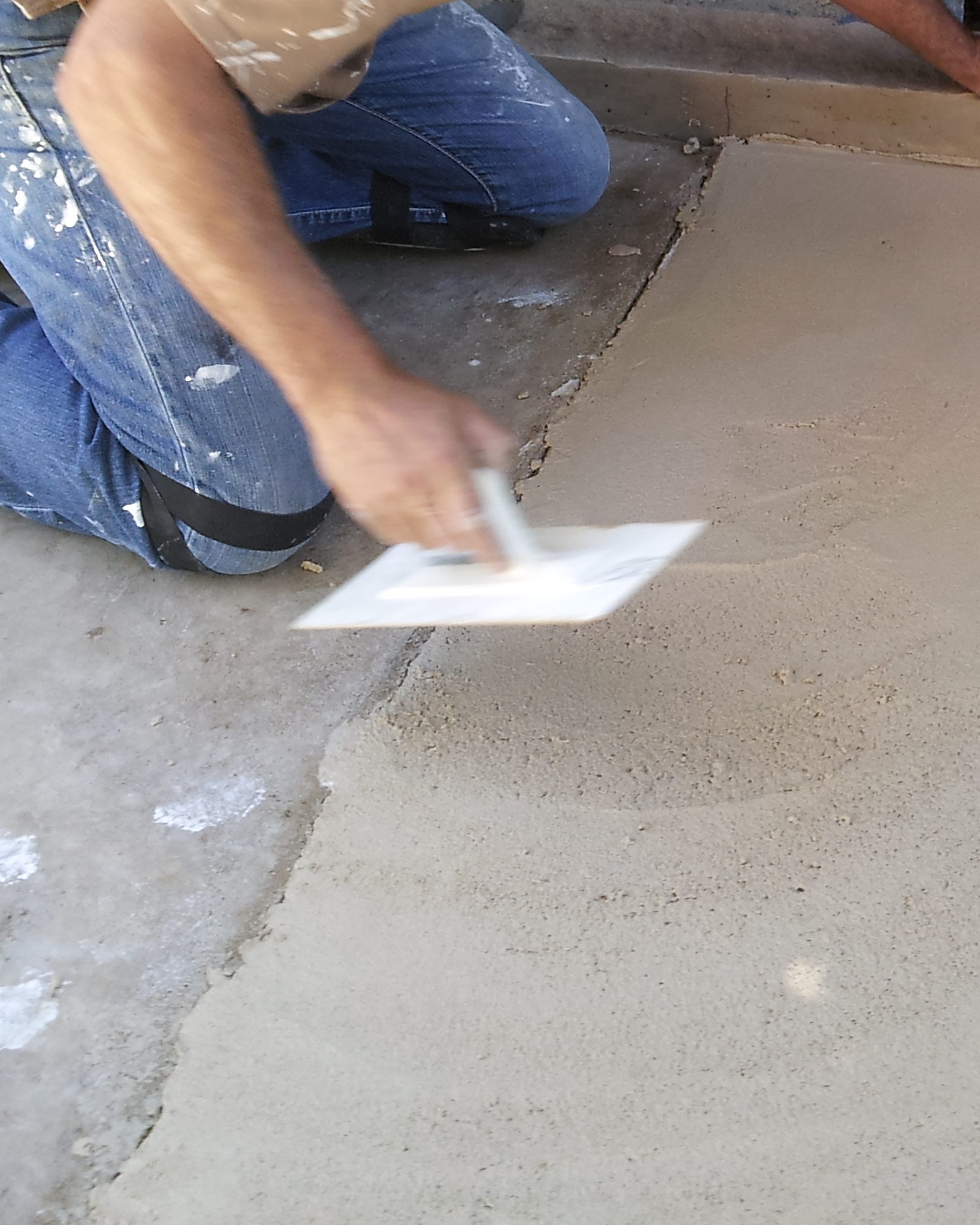 An applicator's hands floating a fresh coating on a slab.