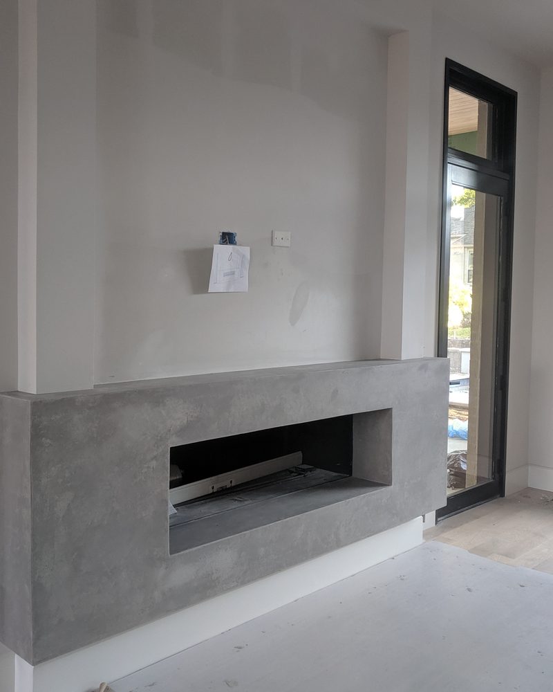 A grey coated fireplace wall mid-installation, the floor protected.