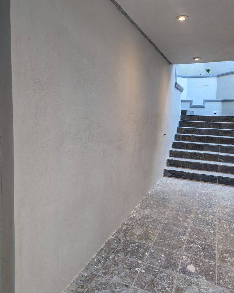 An exterior passage wall in smooth coated stone beside a stair.