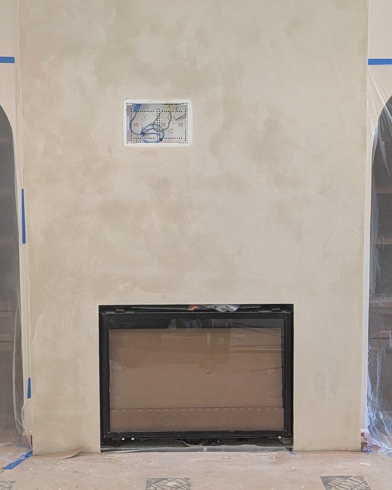 A coated fireplace wall with the room masked and sheeted for the work.