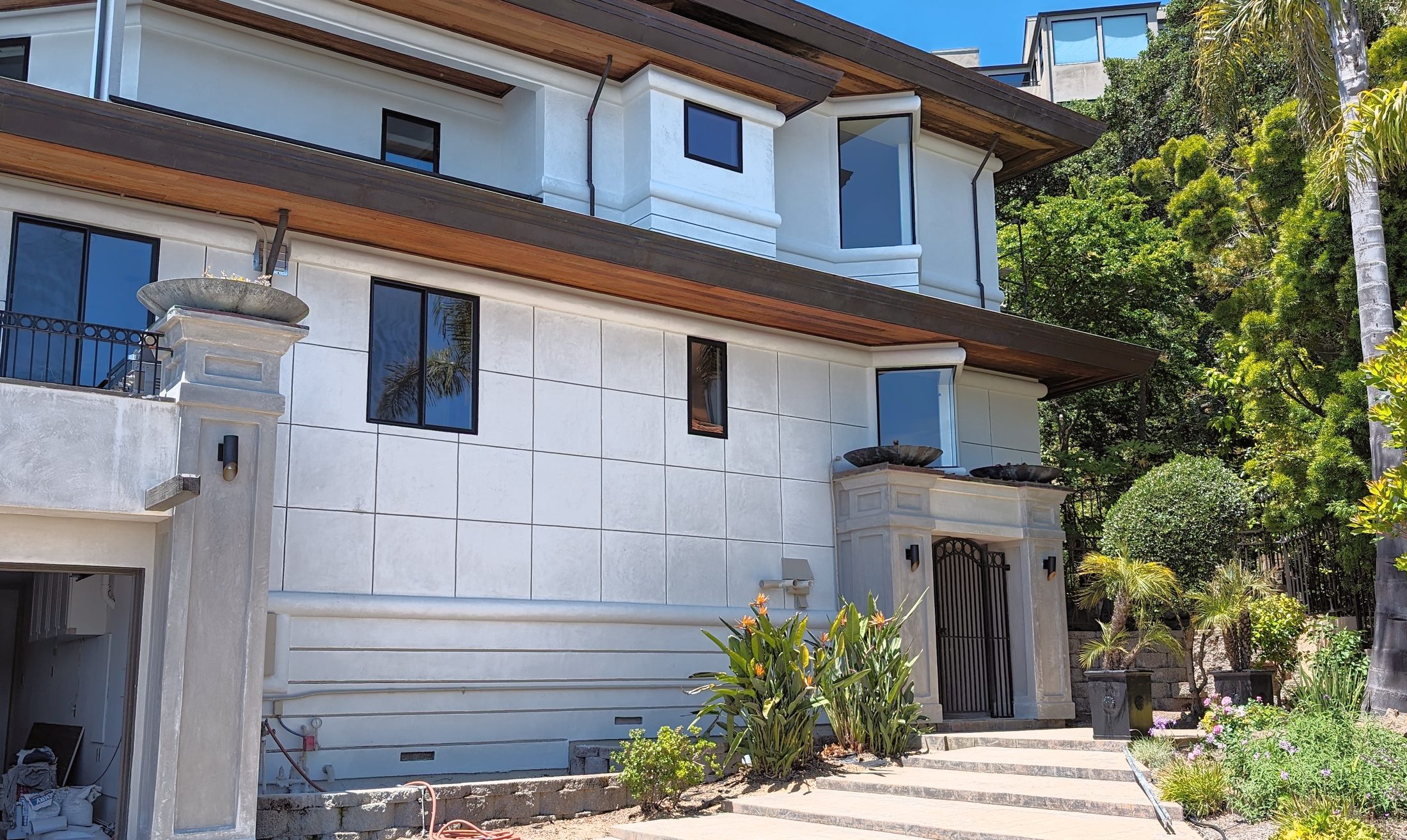 A modern two-storey residence in white coated stone with dark trim.